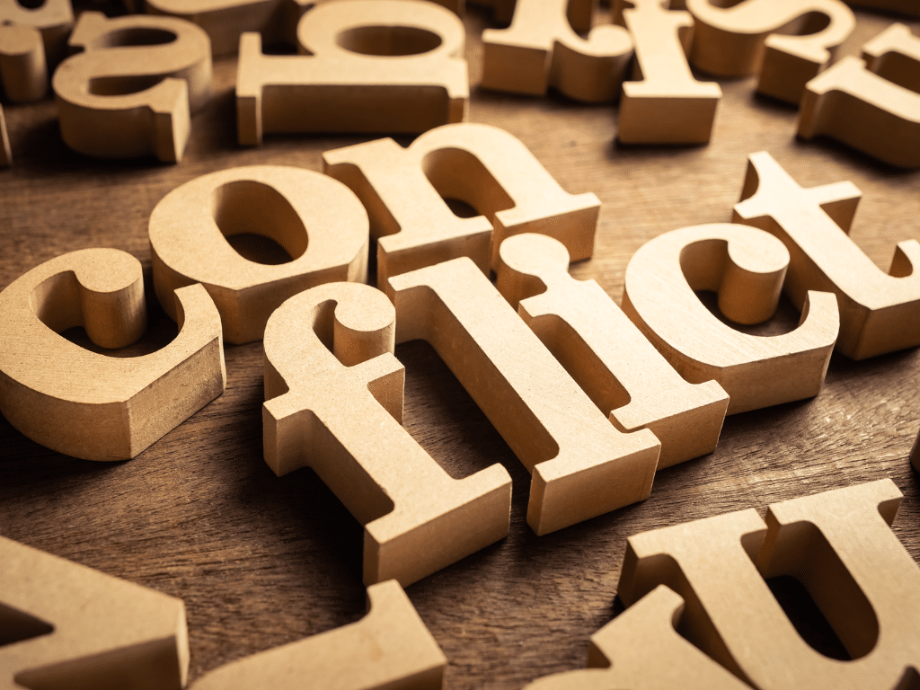 An image of the word conflict in wooden letters.